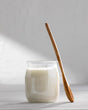 A glass jar filled with milk curd, with a wooden spoon leaning over it.